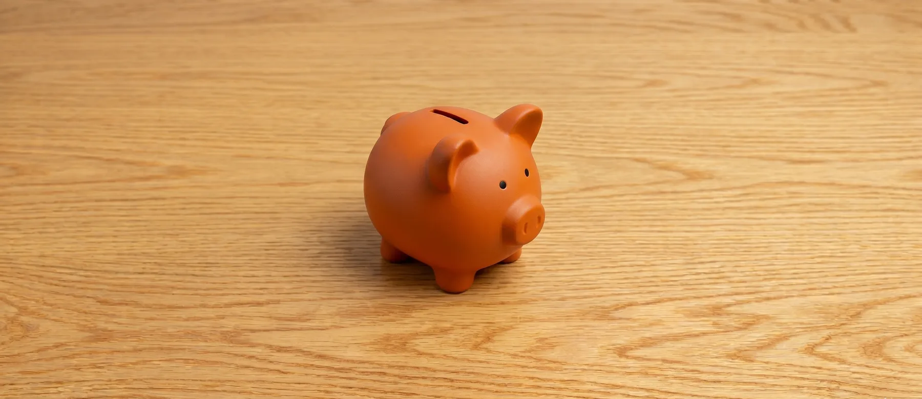 A terracotta piggy bank on a warm wooden desk