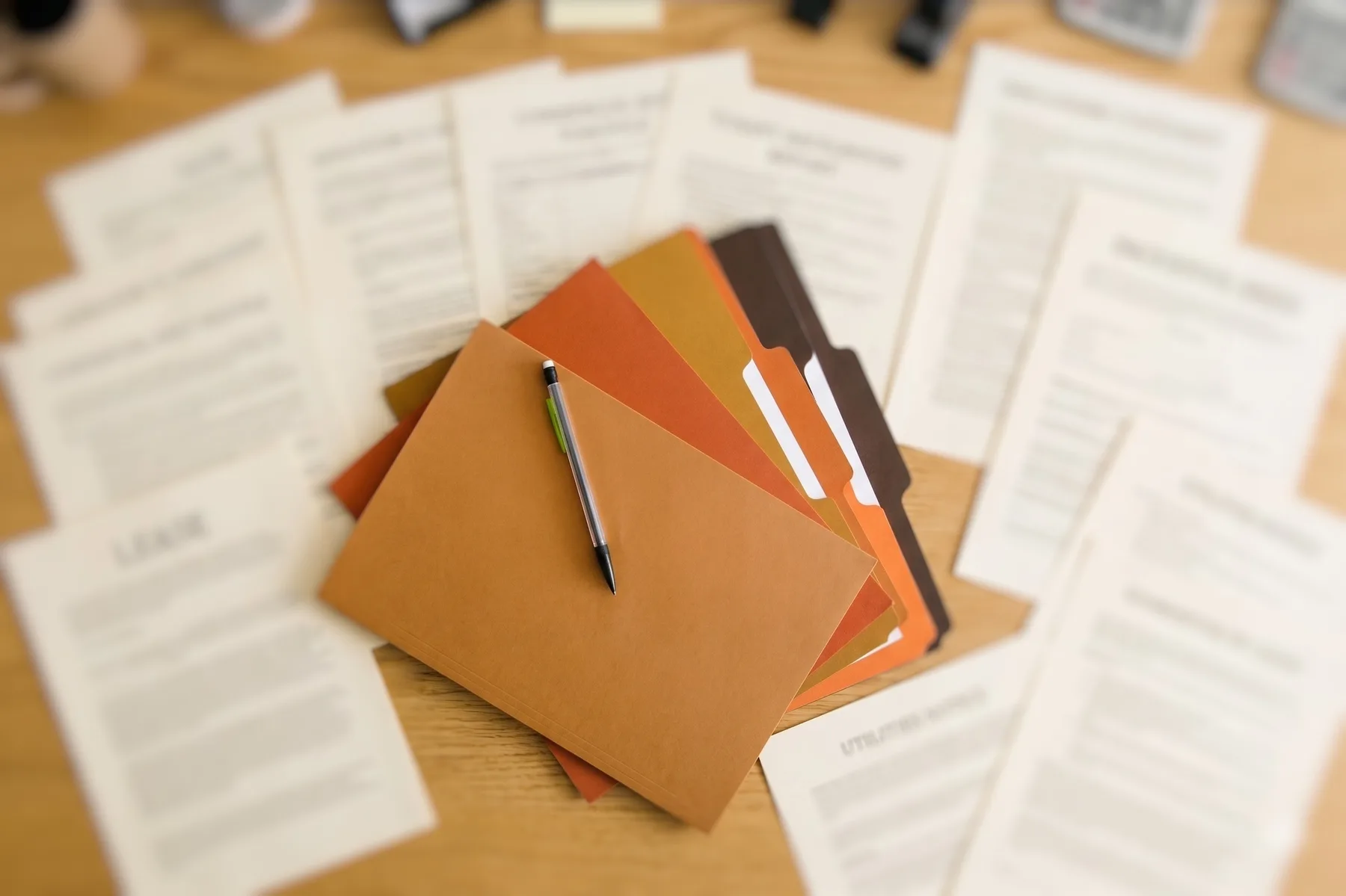 Coloured file folders fanned out with a pen, surrounded by lease documents on a wooden desk
